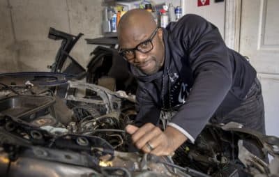 Rich Benoit reaches inside a damaged Tesla he's working on in his garage. (Robin Lubbock/WBUR)