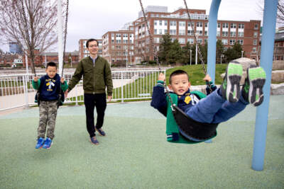 Yang Cao pushes his sons Zhentao and Yiteng on the swings at Menino Park in Charlestown. (Robin Lubbock/WBUR)