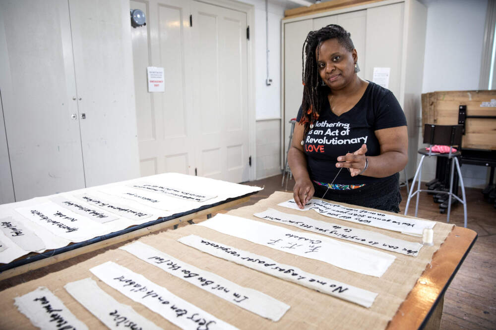 Artist Tanya Nixon-Silberg sews a phrase heard in childhood to a burlap tapestry for "Mother Tongue." (Robin Lubbock/WBUR)