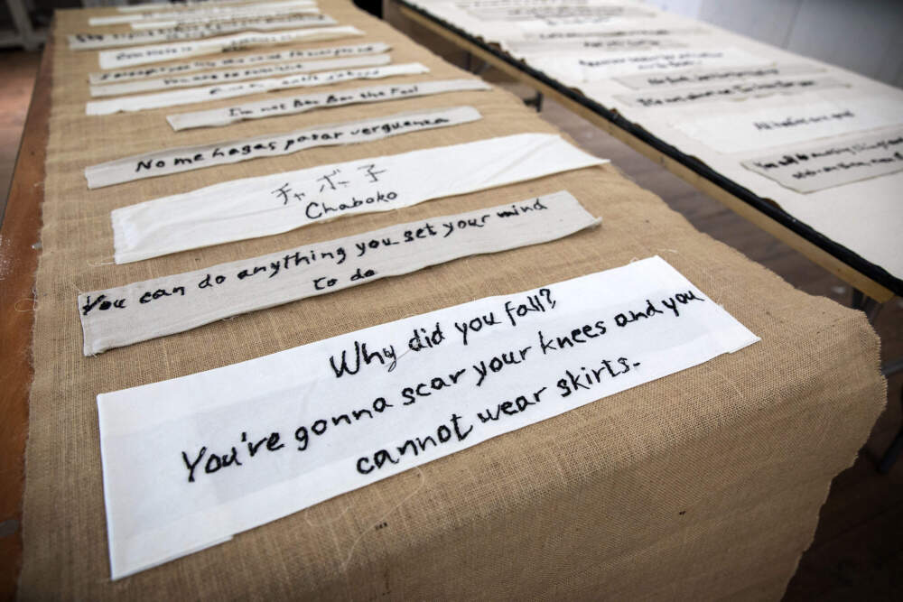 Artist Tanya Nixon-Silberg's &quot;Mother Tongue&quot; shows phrases heard in childhood on a burlap background, and phrases heard today on a muslin background. (Robin Lubbock/WBUR)